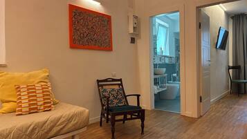 Un salon avec un canapé, un fauteuil, un tableau et une vue sur la salle de bain.