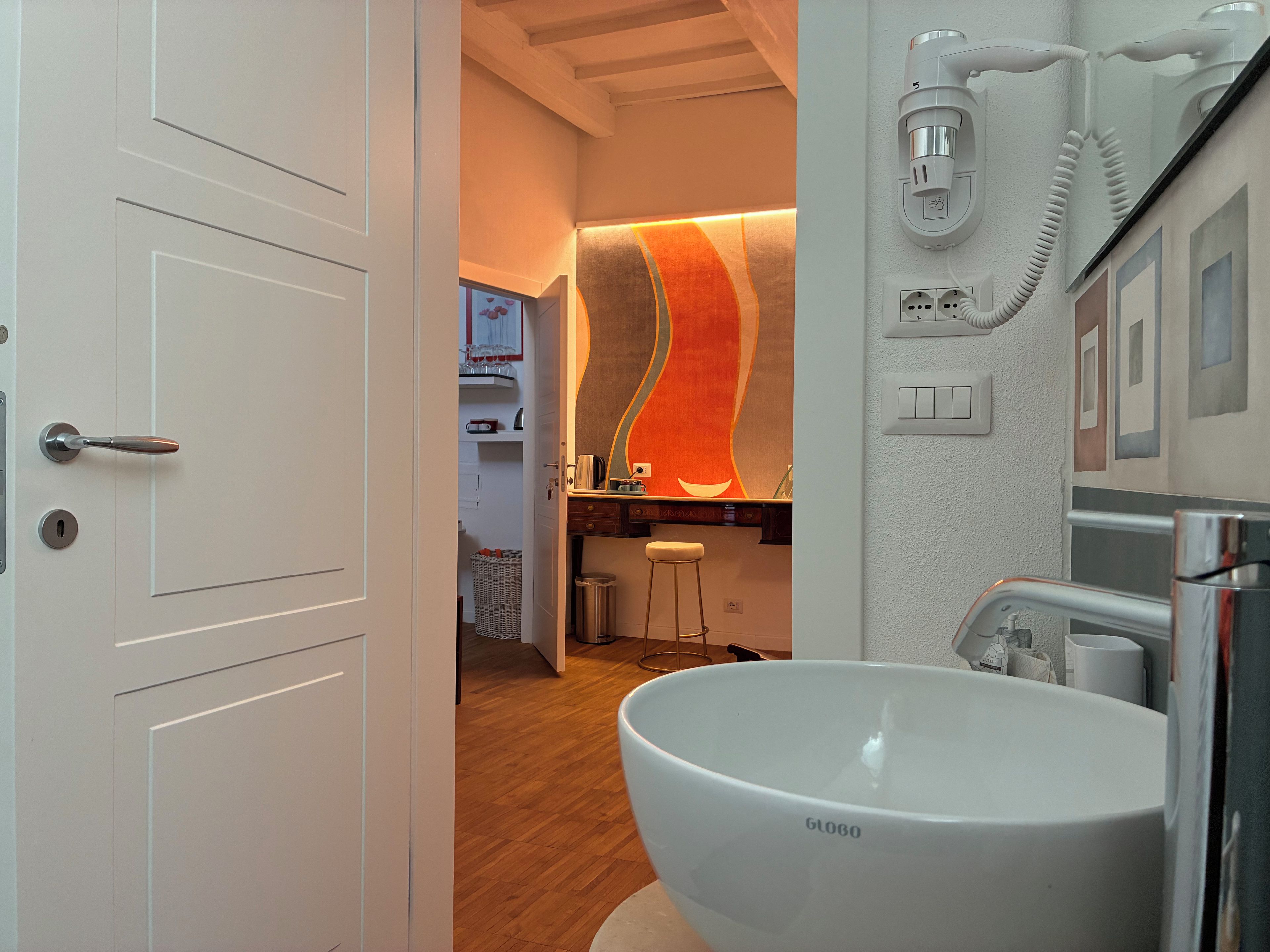 A modern bathroom with a large white basin, a wall-mounted phone, and a wooden floor.