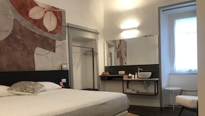 A modern bedroom with a large bed, a bedside table, a mirror, a bathroom with a sink, and a window. - DIMOR'A'   ROOMS (Pitigliano)