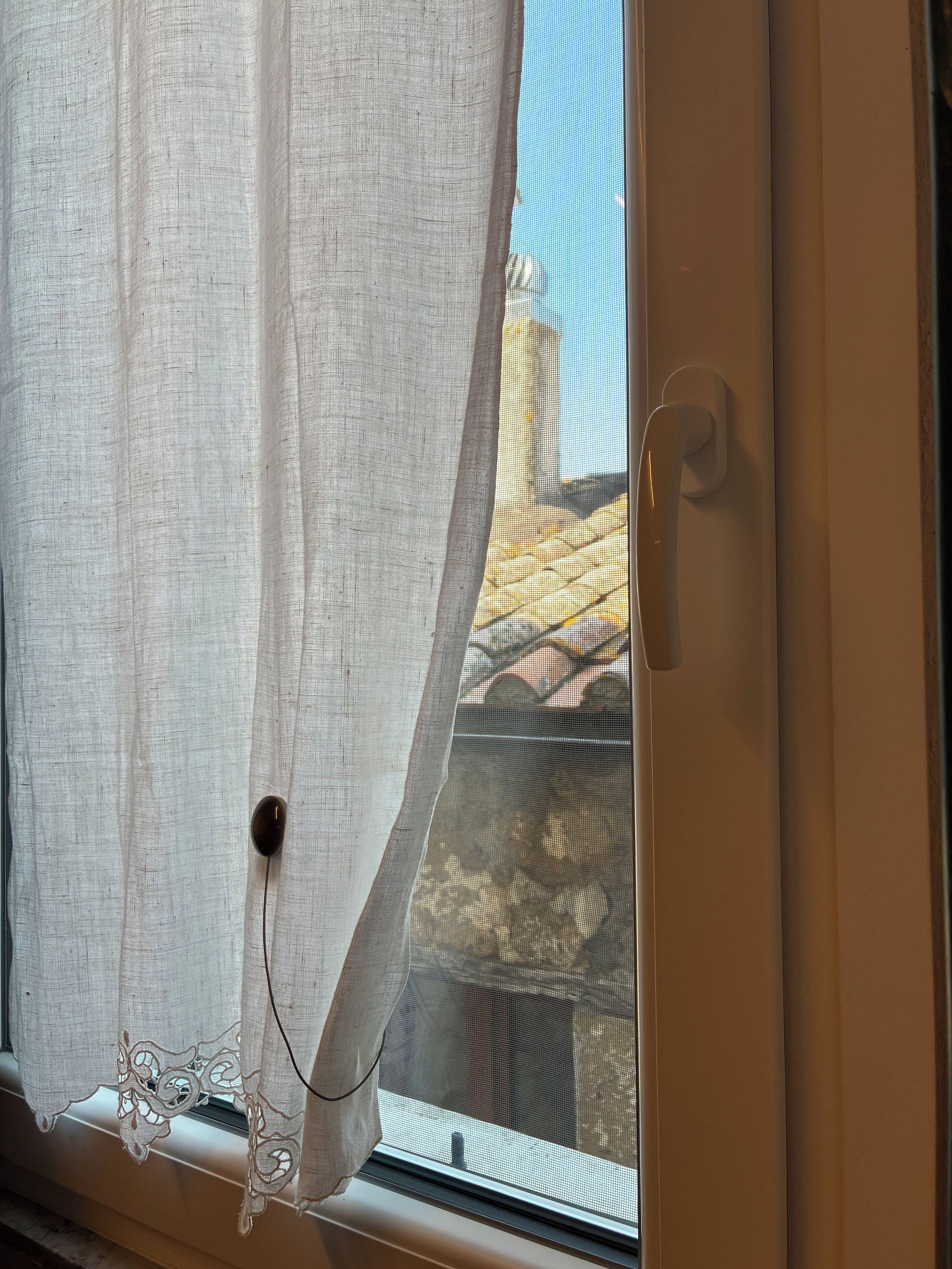 A window with a curtain partially drawn, revealing a view of a building outside.