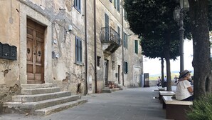 A stone-paved street with a building featuring a wooden door and green shutters. - DIMOR'A'   ROOMS (Pitigliano)