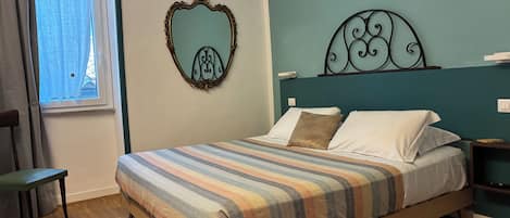 Un dormitorio con cama, una ventana con cortinas, una silla y una pared con espejo decorativo y cabecera.
