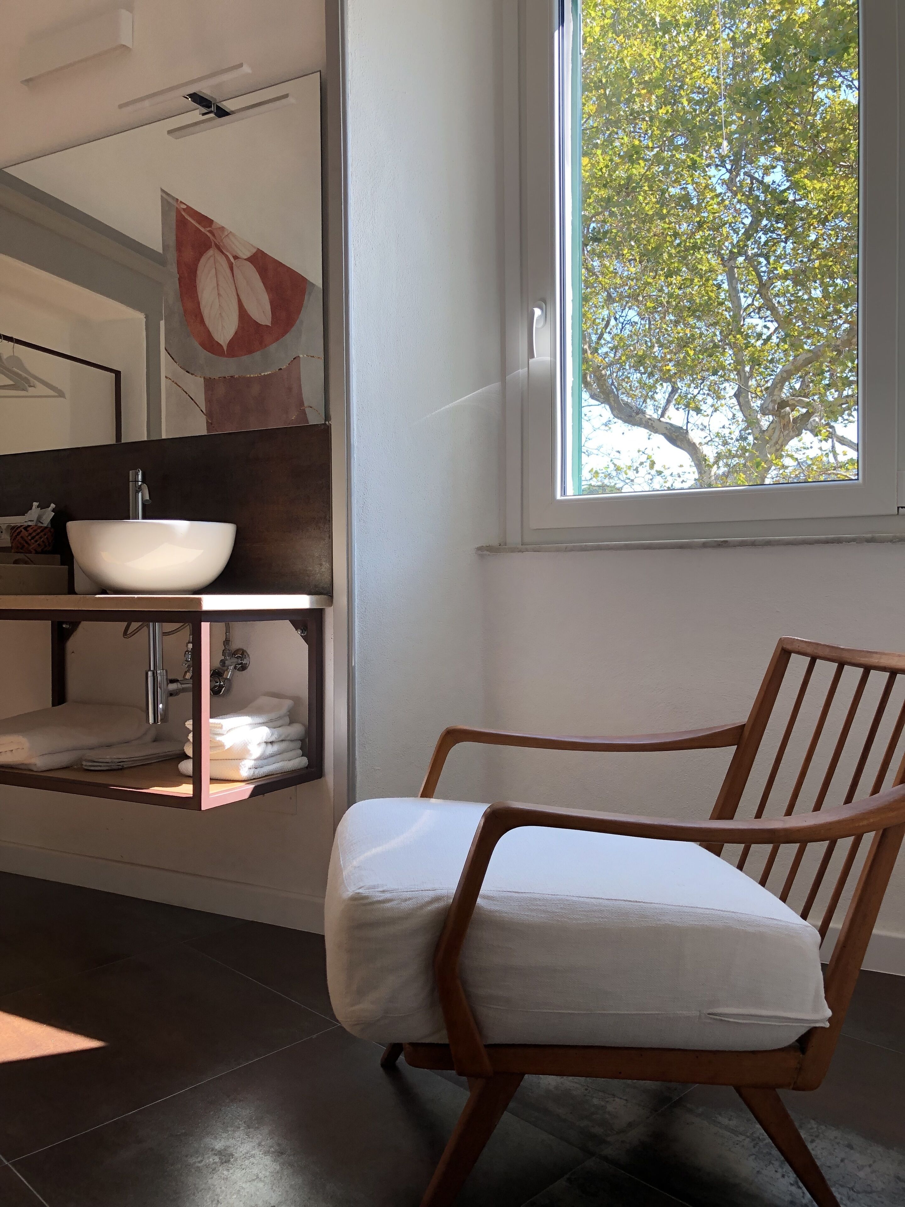 A bathroom with a wooden chair, a white sink, and a window with a tree view.