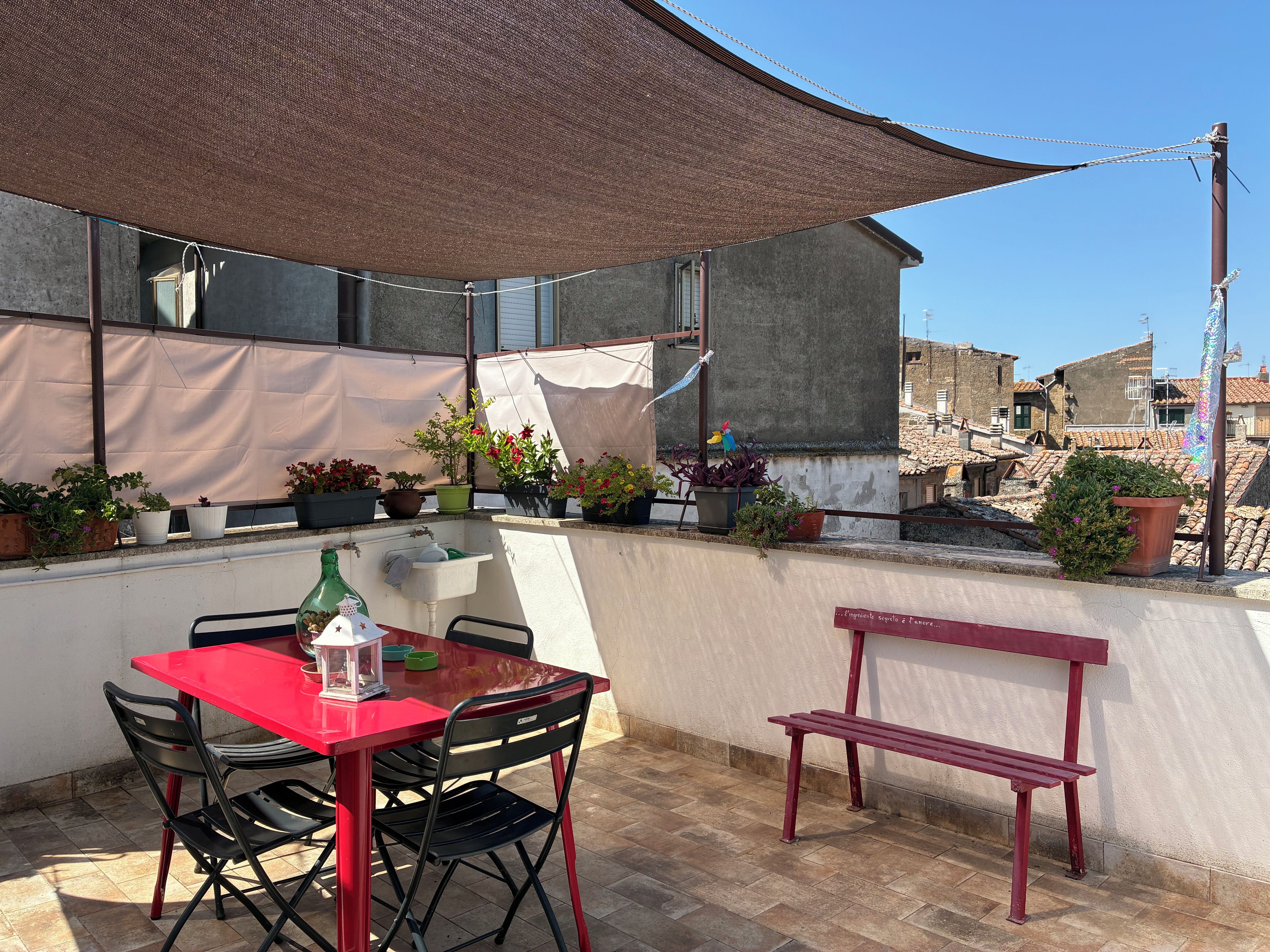 An outdoor patio with a red table and chairs, a bench, and various potted plants.