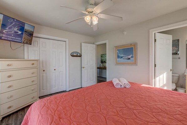 A bedroom with a bed, a ceiling fan, a dresser, and a television on the wall.