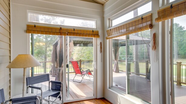 A room with a sliding glass door leading to an outdoor deck, a folding chair, and a table.