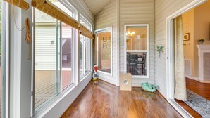 A spacious hallway with wooden flooring, large windows with blinds, and a view into a dining area.