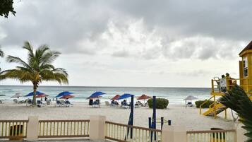 A beach with umbrellas and lounge chairs, a lifeguard tower, and a palm tree.