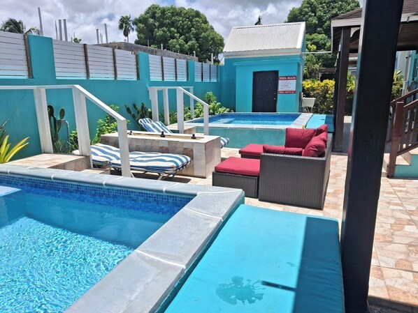 Un espace piscine avec des chaises longues et un petit bâtiment sur lequel est inscrit : « RÈGLES DE LA PISCINE ».