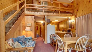 A wooden cabin interior with a dining area, kitchen, and a staircase leading to a loft bedroom. - 'Buckhorn' - Slopeside Iron River Cabin w/ Sauna (Iron River)