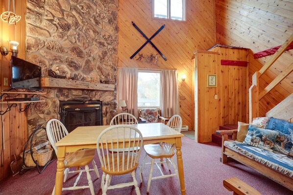 Un acogedor interior de cabaña con pared de piedra, techo de madera, chimenea, mesa de comedor con sillas y un sofá.