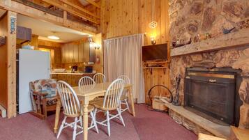 A cozy cabin interior with a dining area, kitchen, and fireplace.