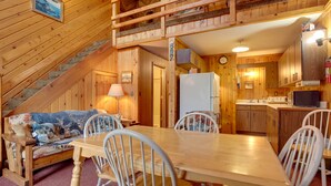 A cozy cabin interior with a wooden staircase, a dining area with a table and chairs, a kitchen with wooden cabinets, and a loft bedroom with a bed. - 'Buckhorn' - Slopeside Iron River Cabin w/ Sauna (Iron River)