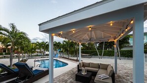 Un espacio al aire libre techado con piscina, sillones de descanso y un sofá.