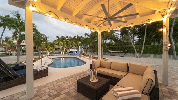 Un espacio exterior techado con piscina, asientos y luces colgantes.