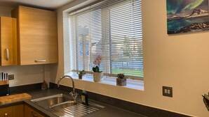 Una cocina con un lavamanos de acero inoxidable, armarios de madera y una ventana con persianas.
