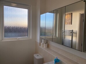 Uma casa de banho com um espelho grande, uma janela com vista e um porta-toalhas.