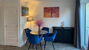 Un comedor con una mesa redonda, sillas azules, un florero con flores rosadas, un cuadro de un árbol y una chimenea.