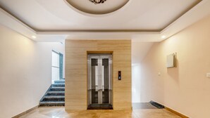 A spacious lobby with a marble floor, a central elevator, and a staircase leading to another level. - Treebo Expo Mart Inn, Greater Noida (Greater Noida)