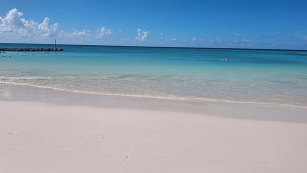 Une plage à l’eau turquoise et limpide, avec un rivage sablonneux et quelques personnes qui se baignent.