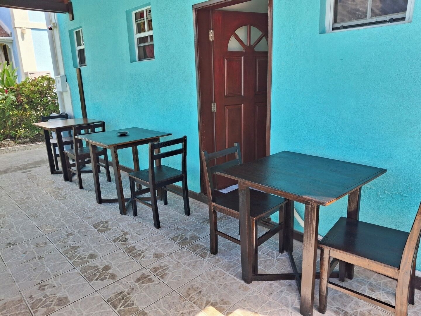 A patio area with wooden tables and chairs, a tiled floor, and a blue wall with a wooden door.