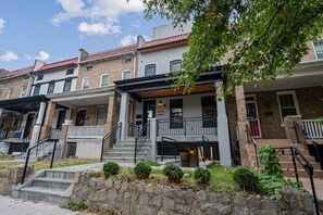 A row of townhouses with brick facades, a central entrance with a covered porch, and a stone retaining wall. - Charming DC Retreat | Perfect for Sightseeing & Corporate Stays (Washington)