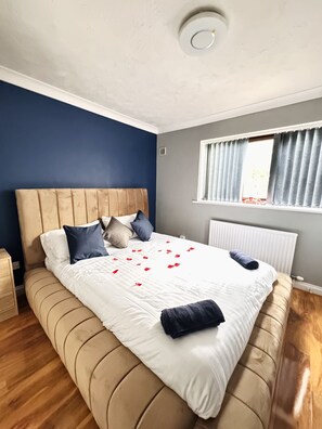 Un lit bien fait, avec une couette blanche, plusieurs oreillers et des pétales de rose éparpillés sur le drap.