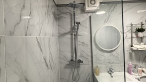 Een moderne badkamer met een douchecabine van glas, marmeren tegels, een ronde spiegel en een wastafel met toiletartikelen.