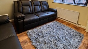 Een woonkamer met een zwarte leren bank, een zachtgrijs vloerkleed en een kroonluchter.