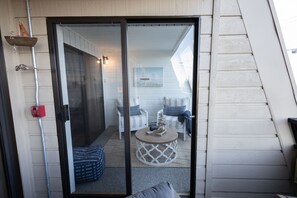 A room with a sliding glass door leading to a balcony with two white chairs and a small round table.