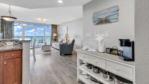 A modern kitchen with a view of the ocean, a dining area with a view, and a living room with a large window. - Ocean View 1BR Condo with Private Balcony (Myrtle Beach)