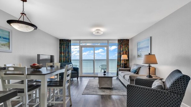 A modern living room with a dining area, a sofa, a coffee table, and a TV. - Ocean View 1BR Condo with Private Balcony (Myrtle Beach)