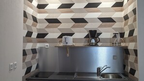 Une cuisine compacte au design moderne, dotée d’un crédence à motifs géométriques, d’un évier encastré et d’un réfrigérateur de petite taille.