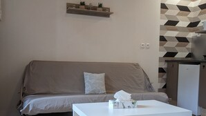 Un petit salon moderne, doté d’un canapé, d’une table basse blanche et d’un coin cuisine avec un revêtement mural à motifs.