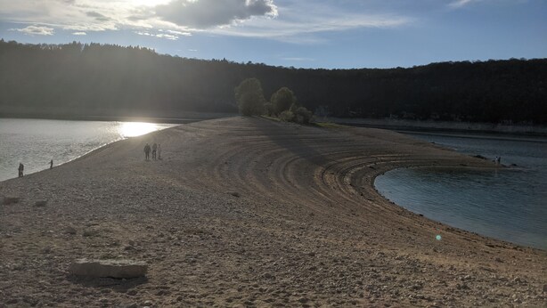 Une plage au rivage incurvé, quelques personnes qui se promènent et, au loin, une colline boisée.