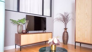 Una sala moderna con un mueble de madera, un televisor de pantalla plana, una mesa de centro redonda de cristal con un florero y un ventanal grande con cortinas.