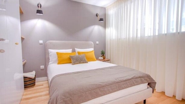 Un dormitorio con cama, cortinas, mesita de noche y lámpara.