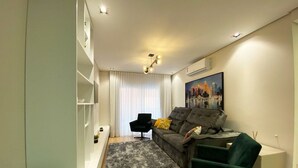 A modern living room with a grey sofa, a green armchair, a black chair, and a painting on the wall.