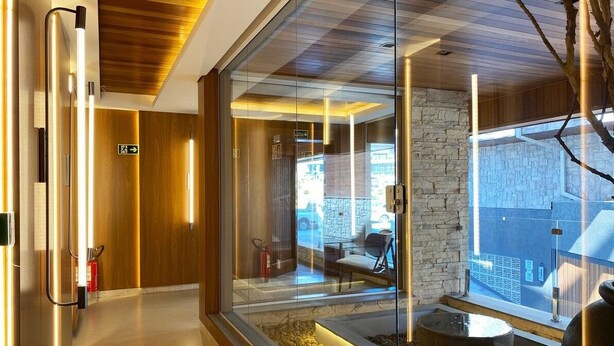 A modern hotel lobby with a glass partition, wooden ceiling, stone wall, and a seating area with a view outside.