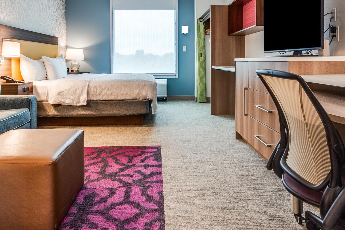Habitación de hotel con cama, escritorio, silla, televisor y vista a la ciudad.