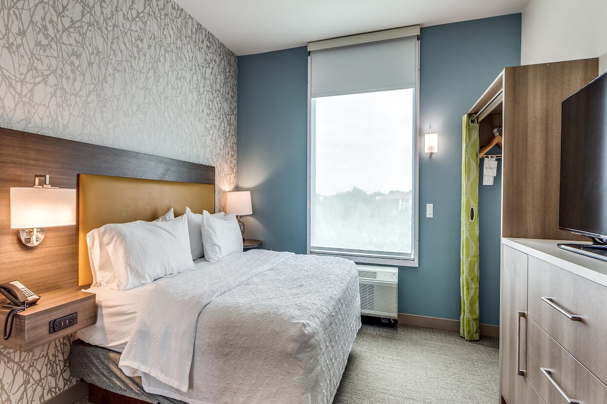 Une chambre d’hôtel avec un lit, des lampes de chevet, un téléphone, une fenêtre donnant sur un paysage agréable et un téléviseur posé sur un meuble.