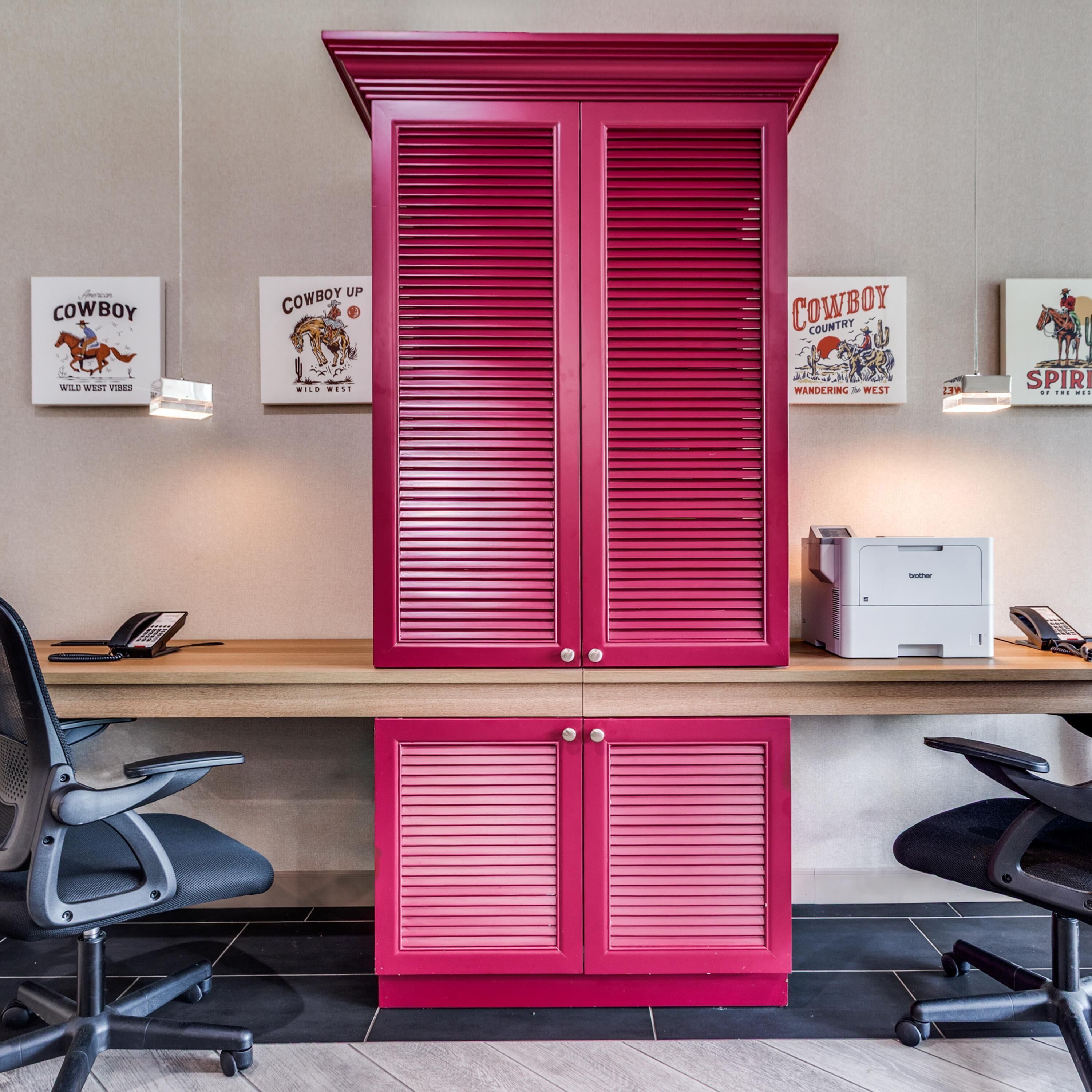 A workspace with a desk, two office chairs, a printer, and three framed posters on the wall.