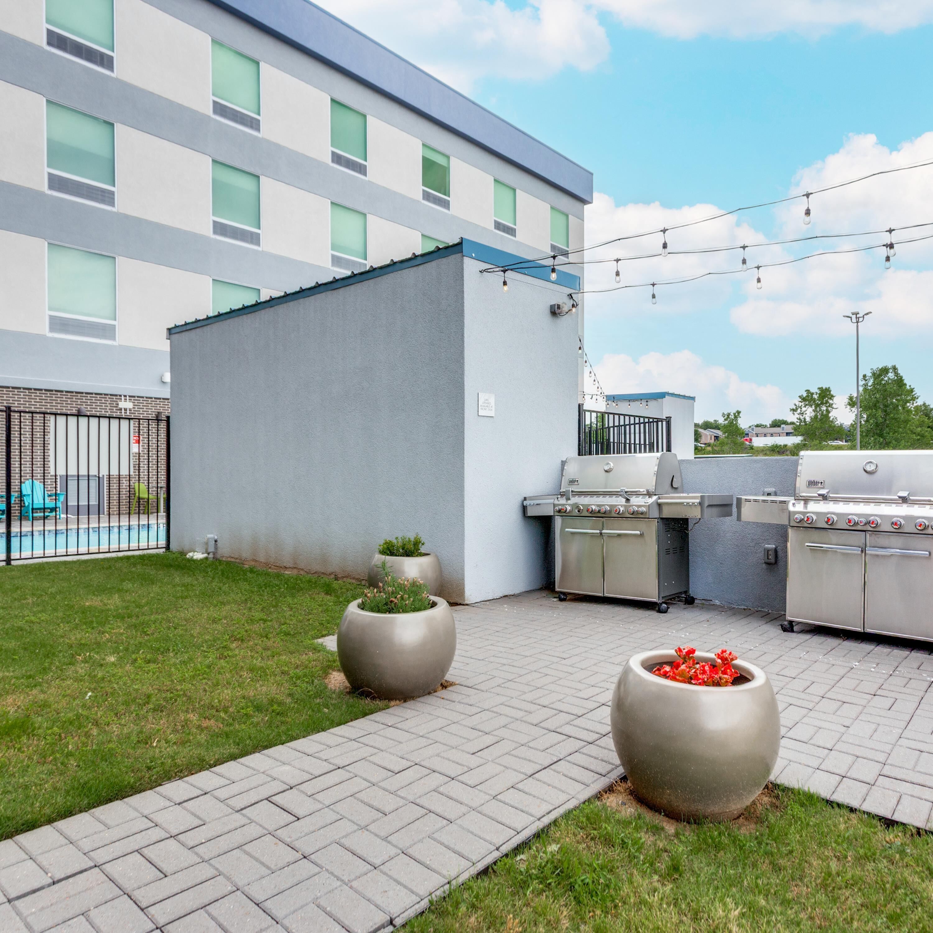 Eine Terrasse mit Grill, Blumentöpfen und einem Pool im Hintergrund.