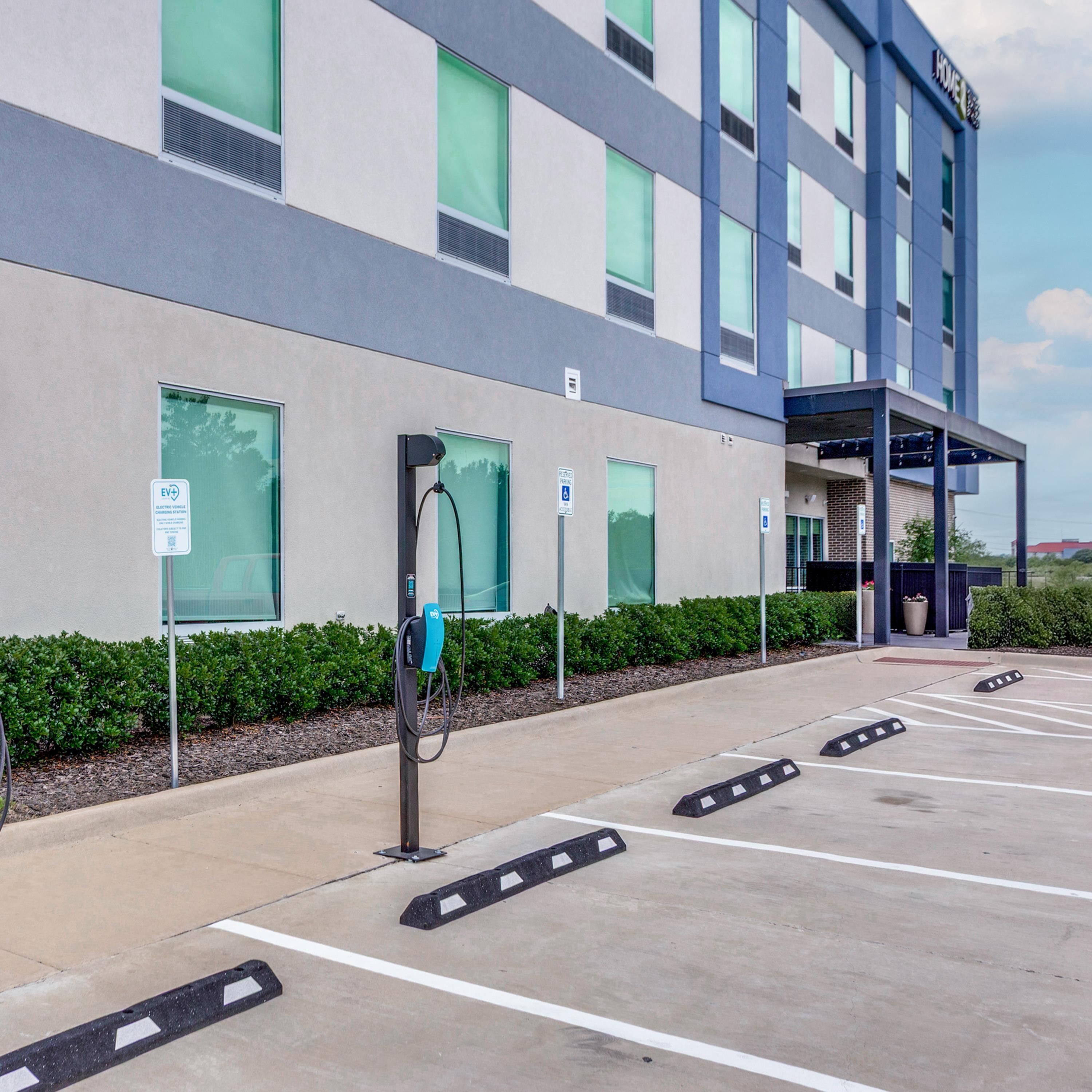 A parking lot with EV charging stations, a building with multiple windows, and a clear sky.