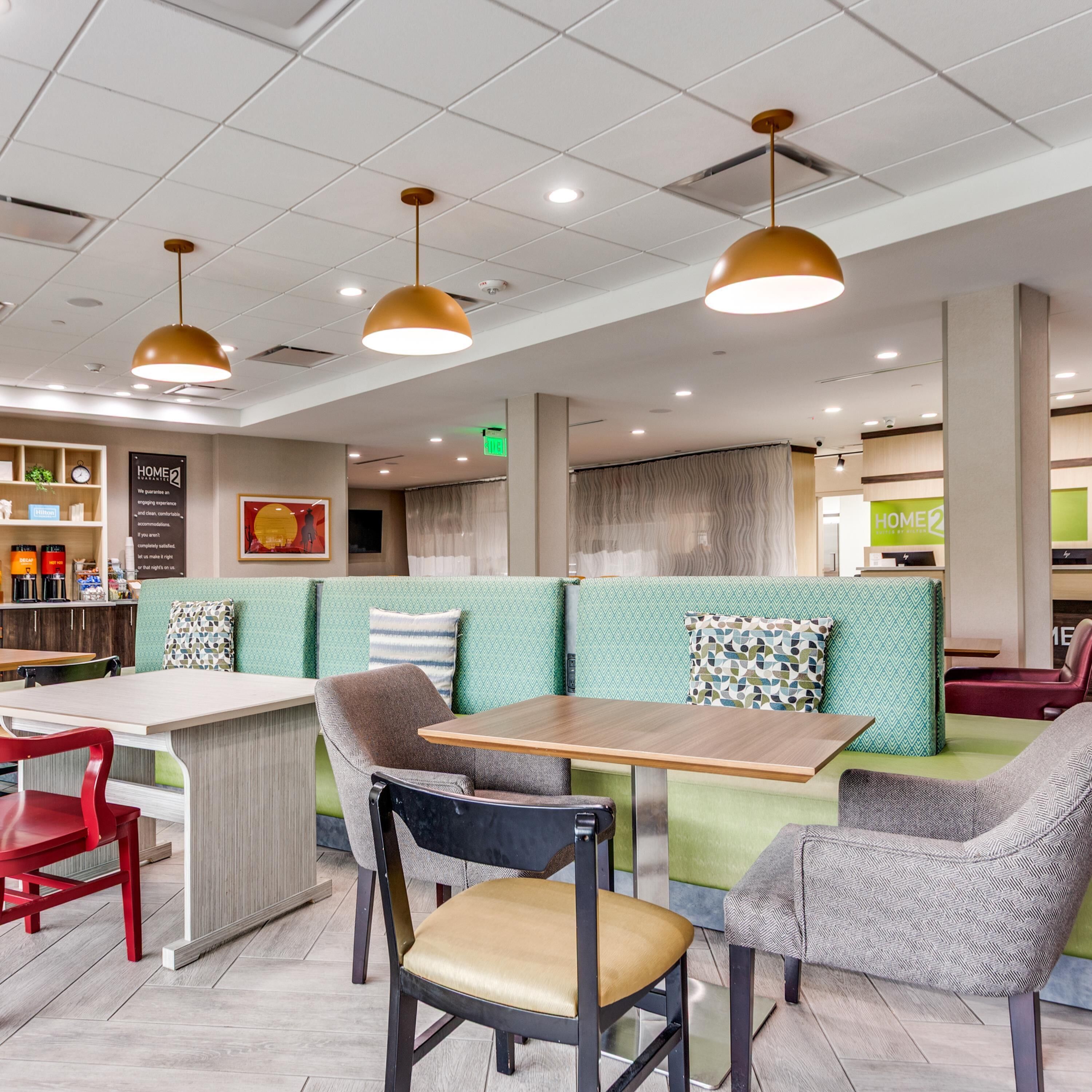 A modern restaurant interior with green seating, wooden tables, and pendant lighting.