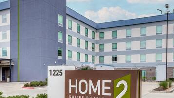 A modern hotel building with a sign reading 'HOME 2 SUITES BY HILTON' and the address '1225'.