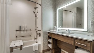 A modern bathroom with a bathtub, shower, vanity with a large mirror, and a towel rack.