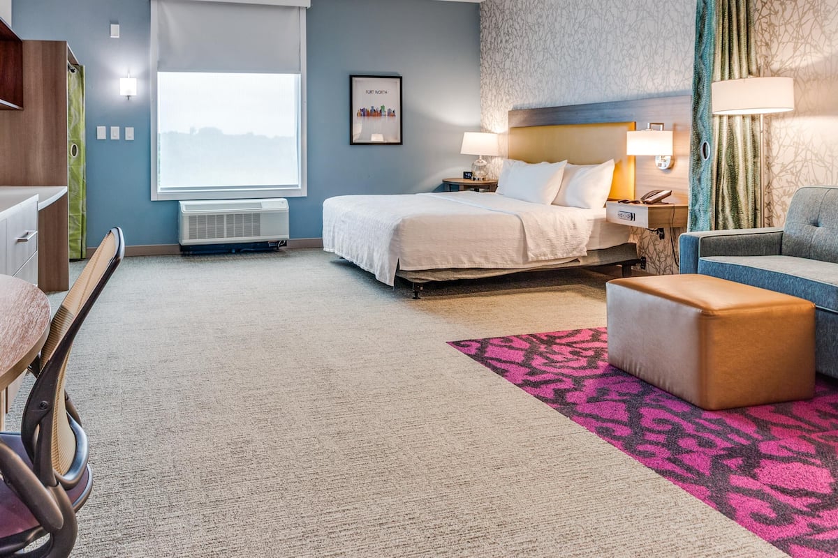 Une chambre d’hôtel avec un lit, un bureau, une chaise, un canapé et un tapis à motifs.