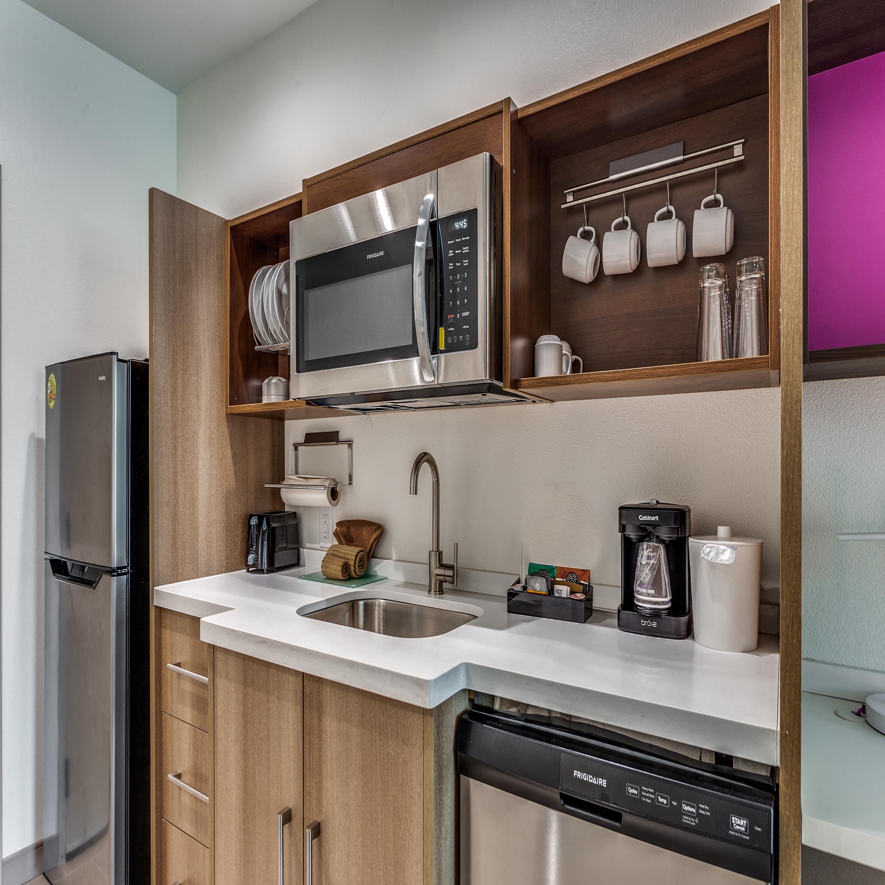 A compact kitchen with a stainless steel refrigerator, a built-in microwave, a coffee maker, and a dishwasher.