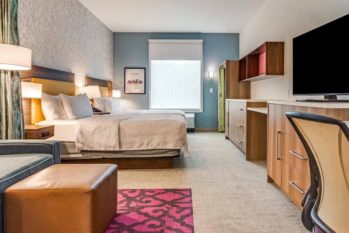 Habitación de hotel con cama, mesitas de noche, escritorio, silla, televisor y ventana.